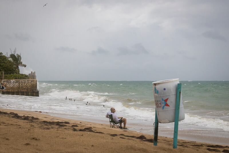 Un hombre se sienta en la playa mientras rompen las olas, antes de la llegada de la tormenta tropical Fiona en San Juan, Puerto Rico, el sábado 17 de septiembre de 2022.