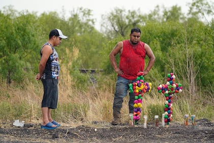 La lluvia cae mientras dos hombres presentan sus respetos en el lugar donde las autoridades encontraron decenas de personas muertas en un semirremolque que contenía presuntos migrantes, el martes 28 de junio de 2022, en San Antonio. (AP Photo/Eric Gay)