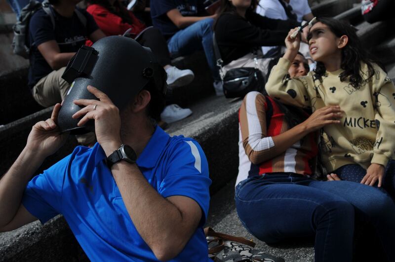 Utilizando una máscara de soldador, una persona observa el avance del eclipse parcial de sol.