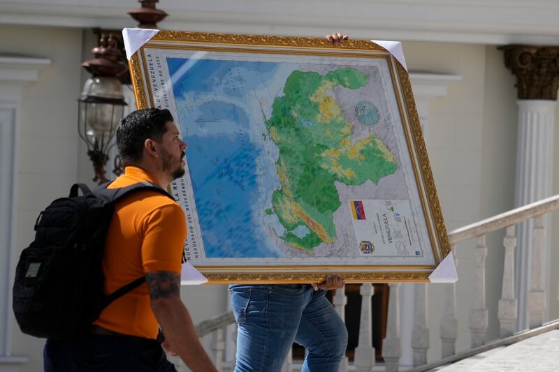 Un hombre lleva el nuevo mapa de Venezuela con el territorio del Esequibo, una gran franja de tierra administrada y controlada por Guyana pero reclamada por Venezuela, al edificio de la Asamblea Nacional en Caracas, Venezuela, el miércoles 6 de diciembre de 2023. (AP Foto/Ariana Cubillos)