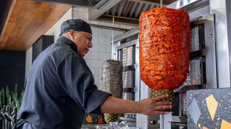 Taquero preparando el trompo de pastor rojo tradicional.